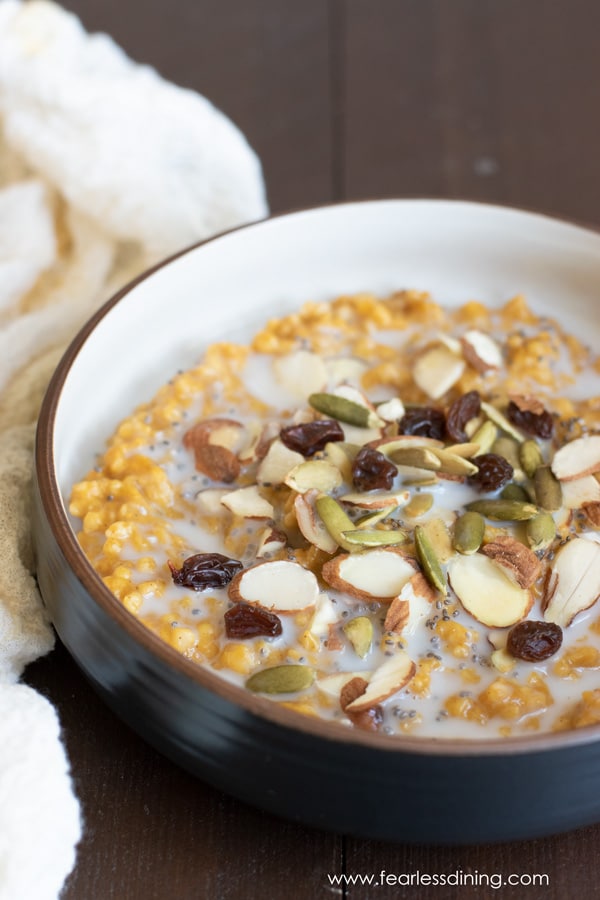 A bowl of slow cooker pumpkin steel cut oats topped with raisins, almonds, and pumpkin seeds.