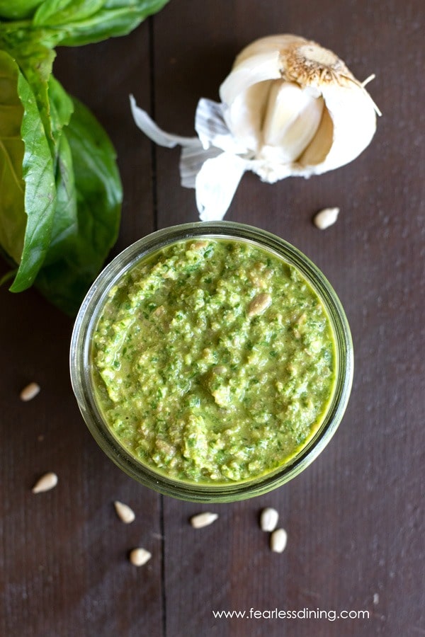 The top view of a jar of nut-free pesto sauce next to a broken garlic bulb.