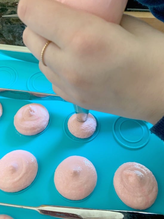 Piping macarons onto a macaron mat.