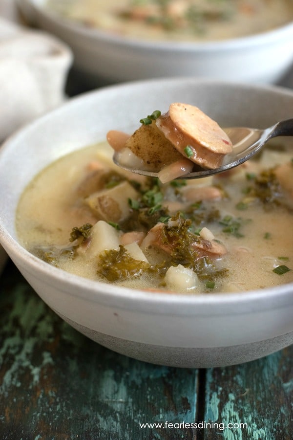 A spoon holding up a cut piece of sausage in the soup.