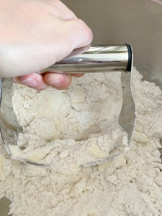 A photo using a pastry blender to cut butter into flour.