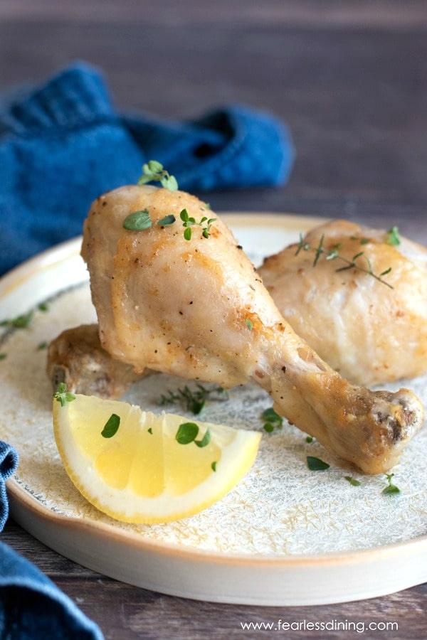 Two gluten free air fried chicken drumsticks on a plate with lemon.