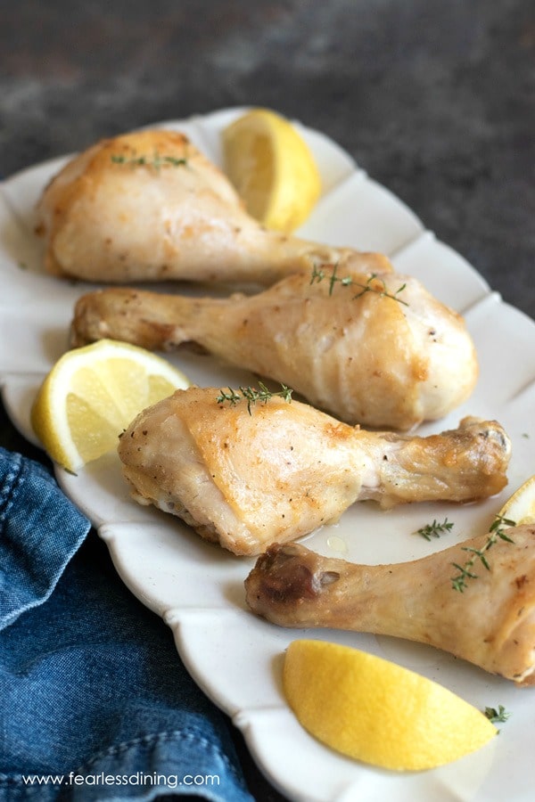 Air fried chicken drumsticks on a platter with cut lemons and fresh thyme.