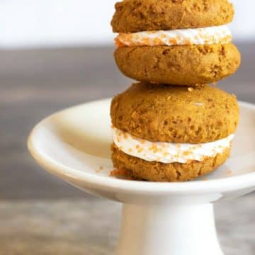 two pumpkin whoopie pies stacked on a white stand.