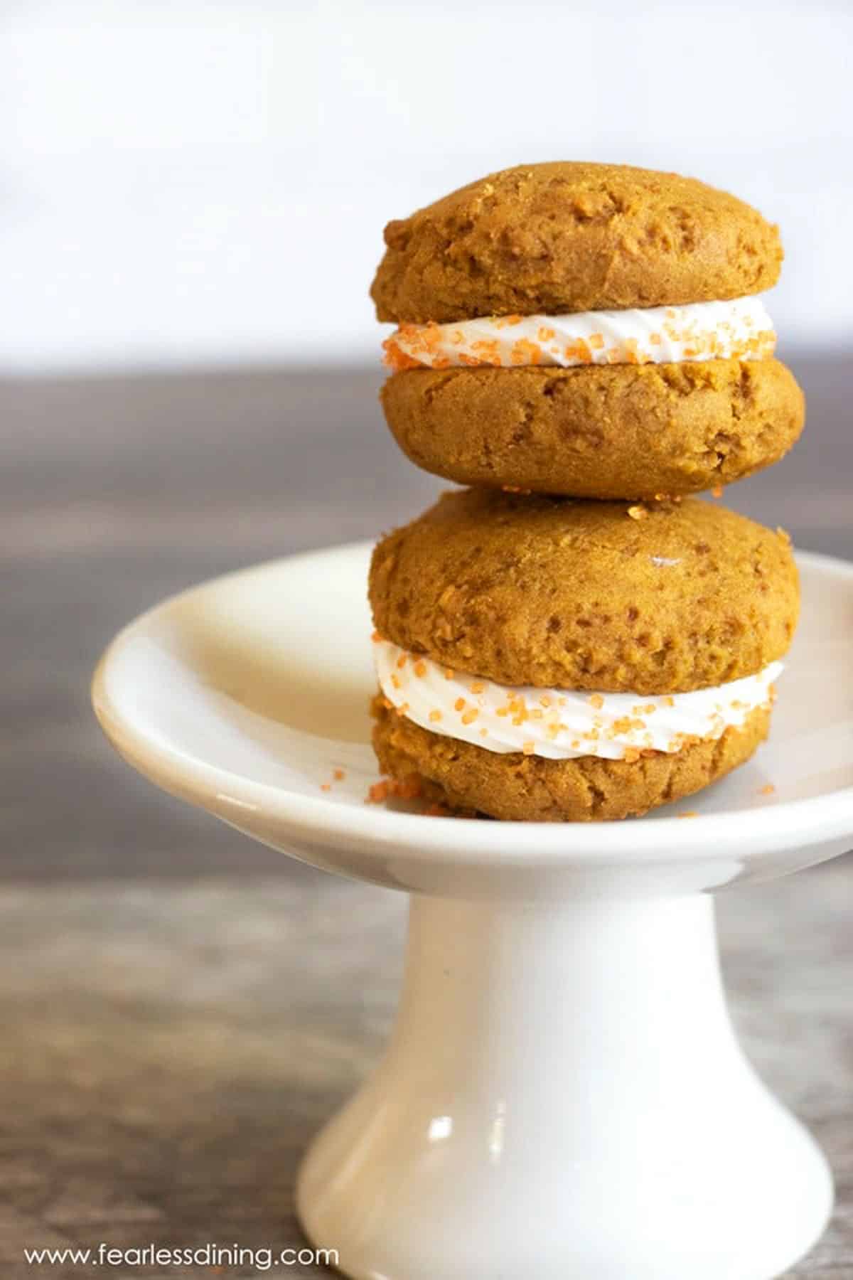 Two pumpkin whoopie pies stacked on a white stand.
