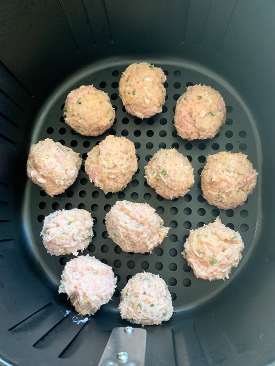 Raw ground chicken meatballs in an air fryer basket.