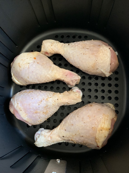 Chicken drumsticks rubbed with spice mix and olive oil in an air fryer.