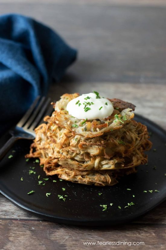 A stack of latkes on a plate. They are topped with sour cream and chives.