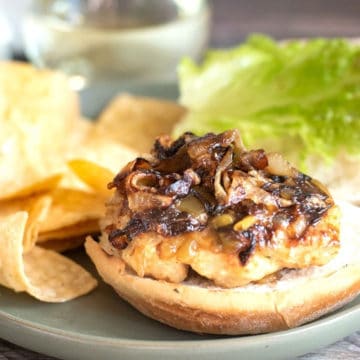 A ground chicken burger topped with caramelized onions and hatch chiles on a bun.
