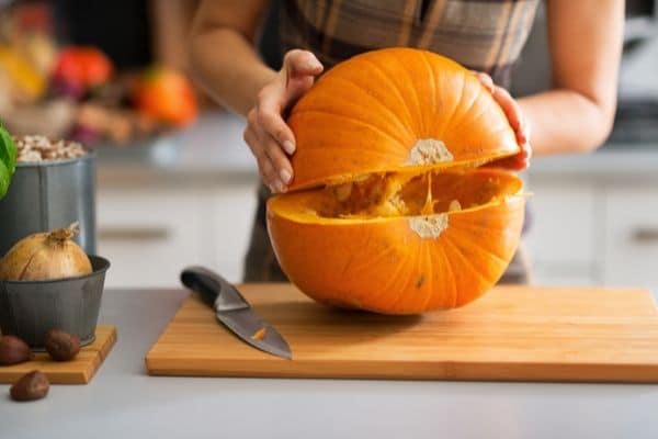 Cutting a pumpkin in half and lifting part to separate it.