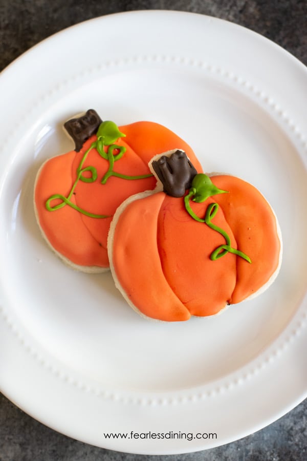 Two gluten free halloween cut out cookies on a plate. They are decorated pumpkin shaped sugar cookies.