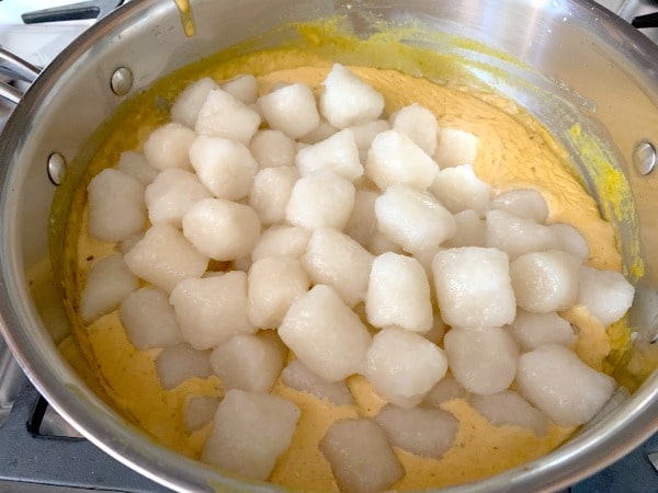 Adding the cooked gnocchi to the pan with pumpkin alfredo sauce.