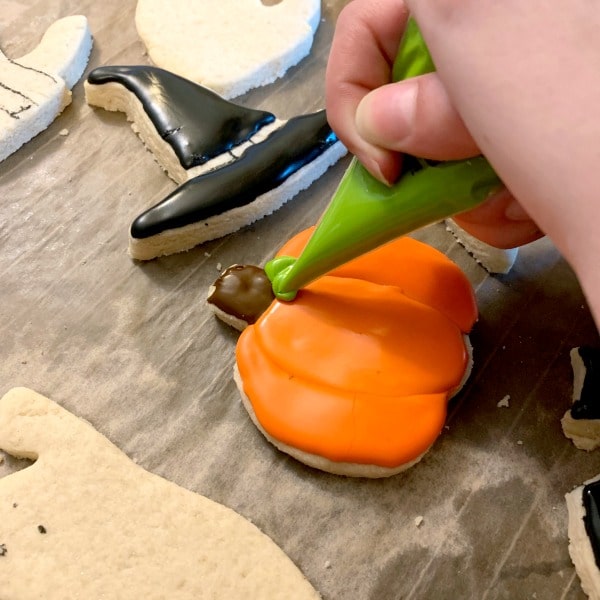 Making a green leaf with icing on a pumpkin shaped cut out cookie.