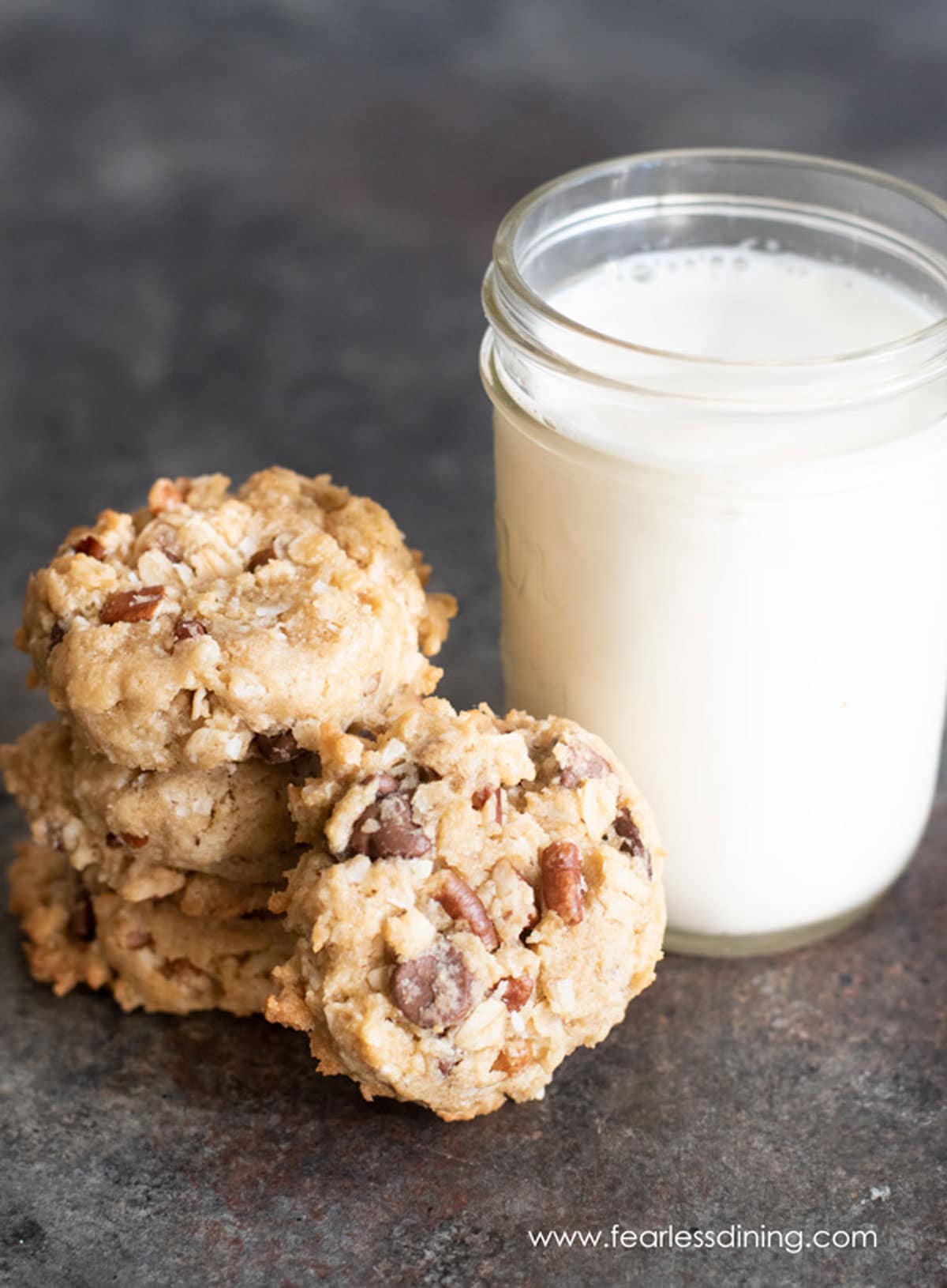 A stack of cowboy cookies next to a glass of milk.