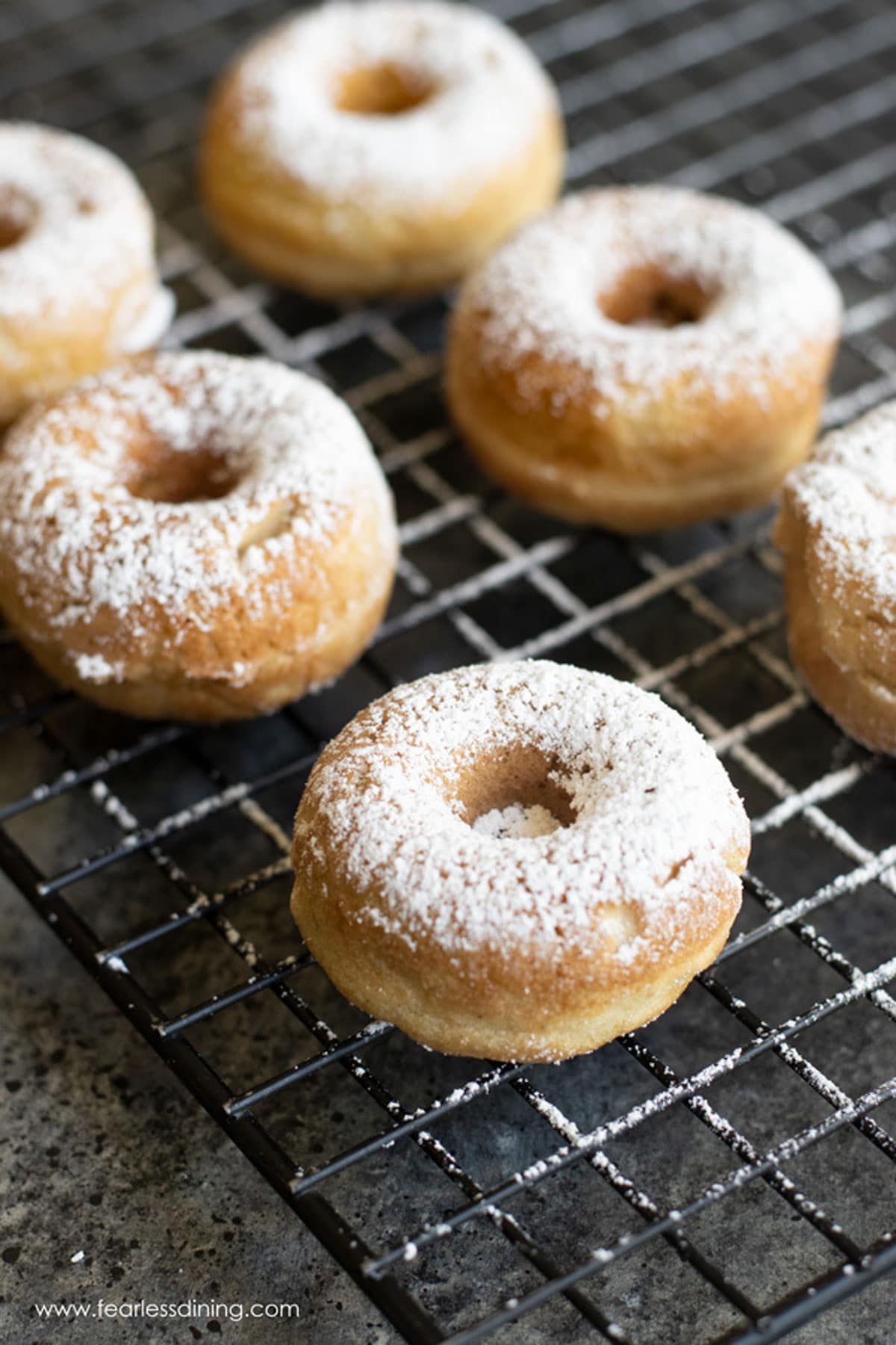 No egg donuts on a rack with powdered sugar dusted over them.