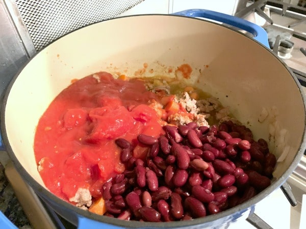 Adding the remaining chili ingredients to the cooked ground pork.