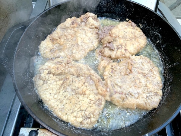 Frying chicken fried steak in a cast iron skillet.