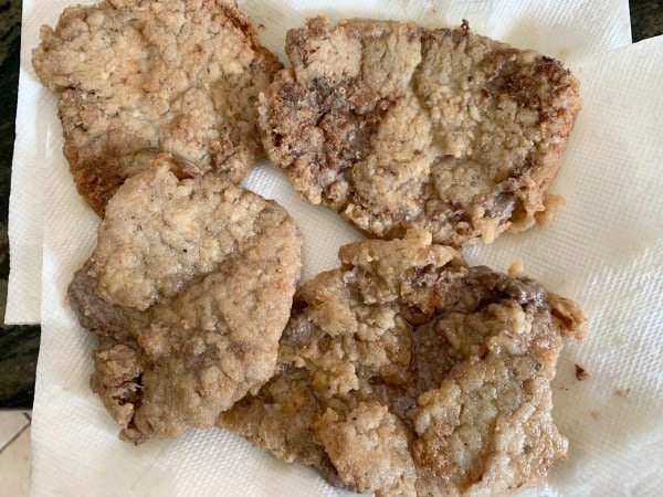 Chicken fried steaks on a paper towel lined plate.