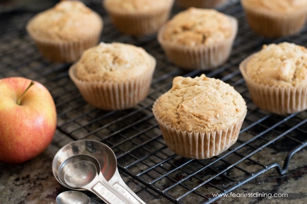 Gluten free apple muffins on a cooling rack next to an apple.