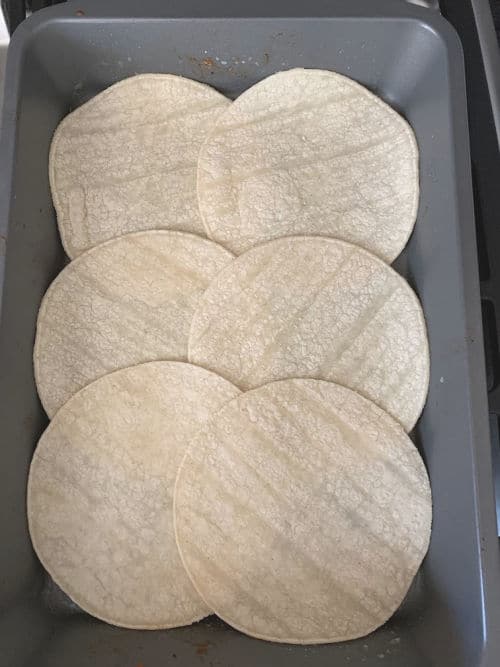 The corn tortillas lining the bottom of a baking dish.