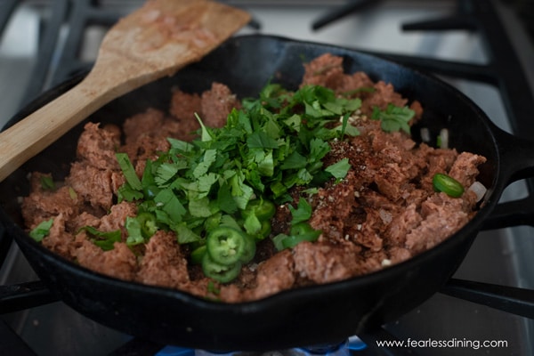 Add spices, jalapeõs, and fresh cilantro to the pan of cooking meat