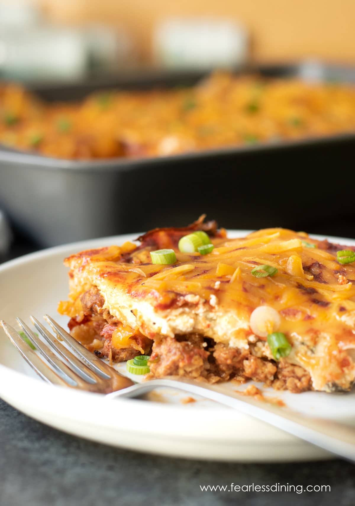 A slice of the vegan Mexican casserole on a plate. A fork is next to the slice.