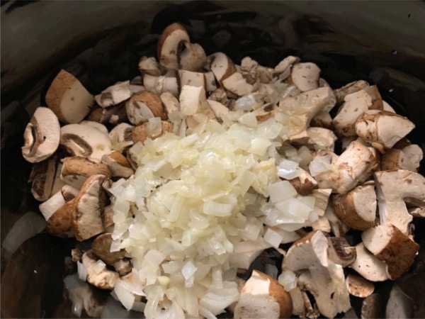 Onion and mushrooms added to the slow cooker.