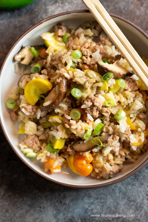 A top view of a bowl of gluten free ground pork fried rice. Chopsticks are sitting on the rim of the bowl.