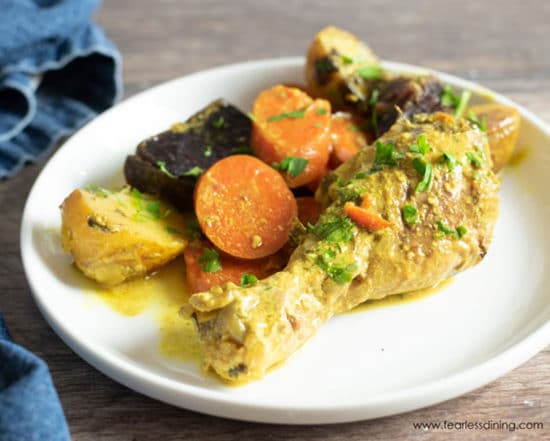 A slow cooker curry chicken drumstick on a plate with vegetables.