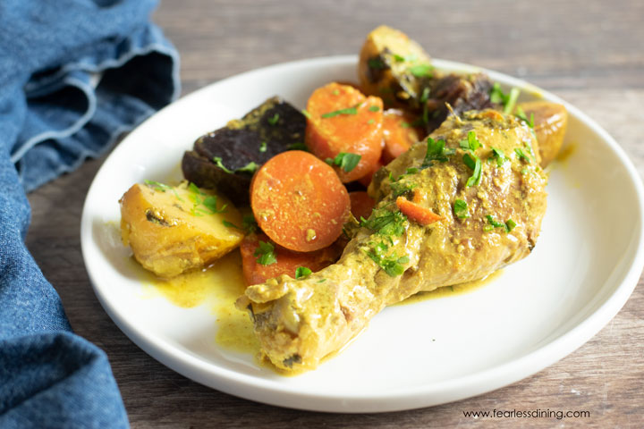 A plate with a curry drumstick next to carrots and potatoes.