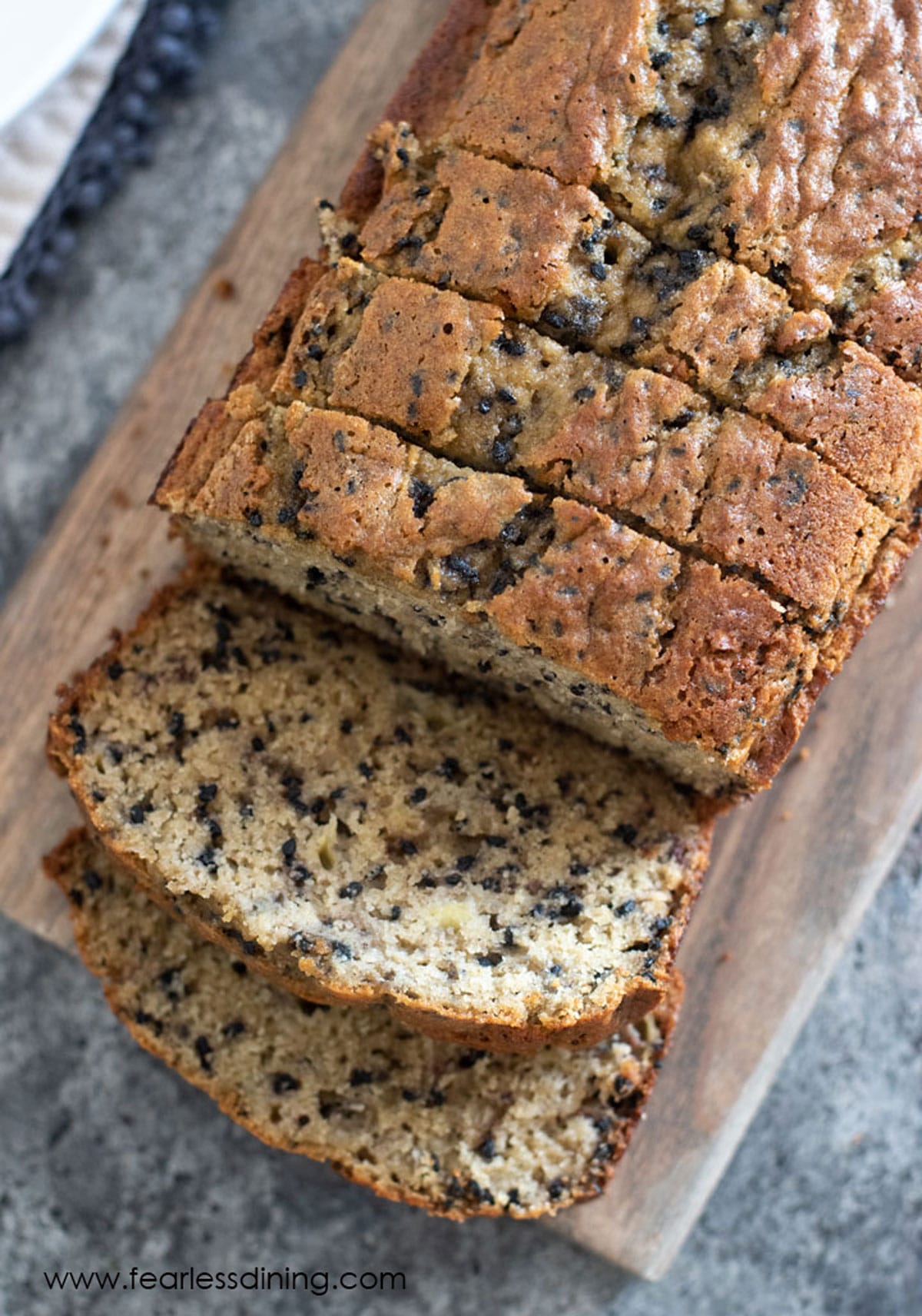 A loaf of gluten free banana sesame bread sliced on a cutting board.