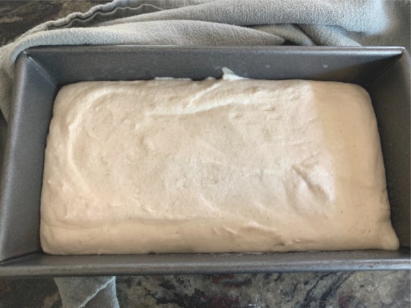 Sourdough bread batter rising in a loaf pan.