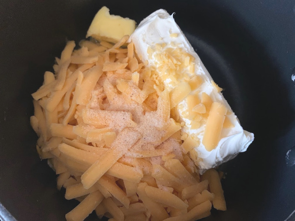 Ingredients for cheese sauce in a pot. Cream cheese, butter, cheddar cheese and seasonings.