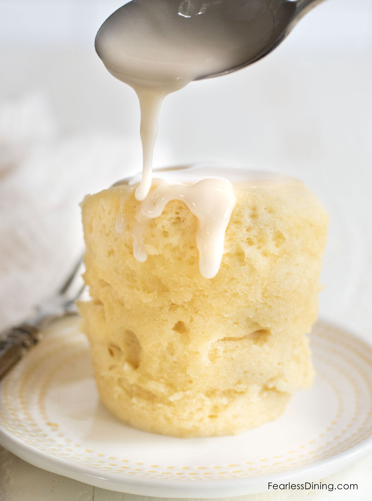 A shot of a spoon drizzling lemonade icing over a microwave cake.