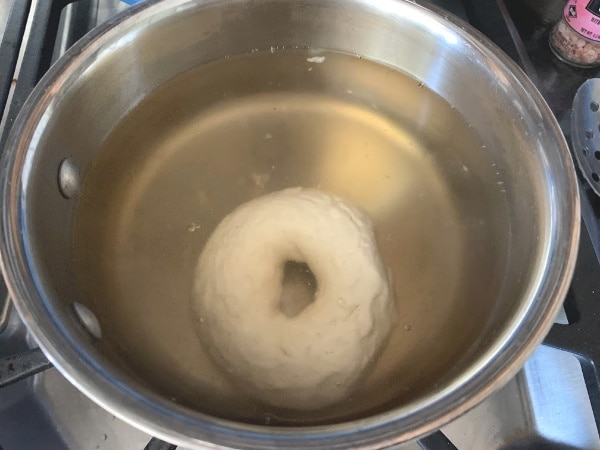 An uncooked bagel in a pot of boiling maple syrup water.