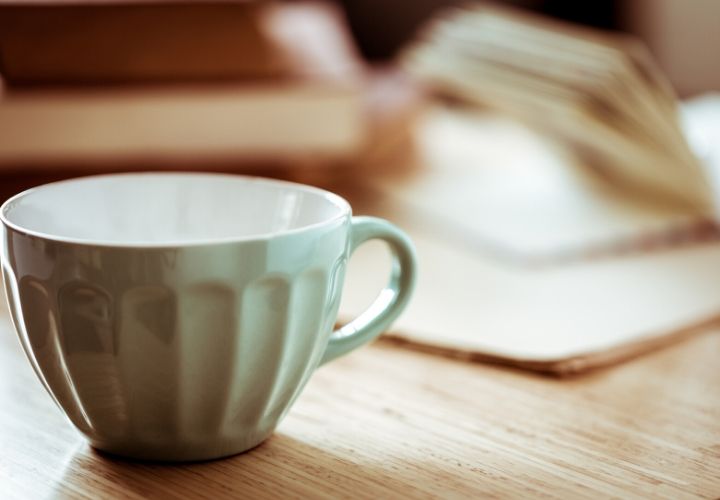 An empty pale green coffee mug near an open book.