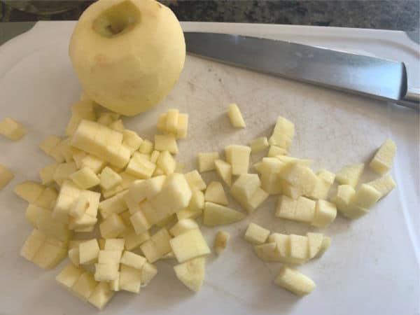 a peeled apple next to diced apples on a white plastic cutting board