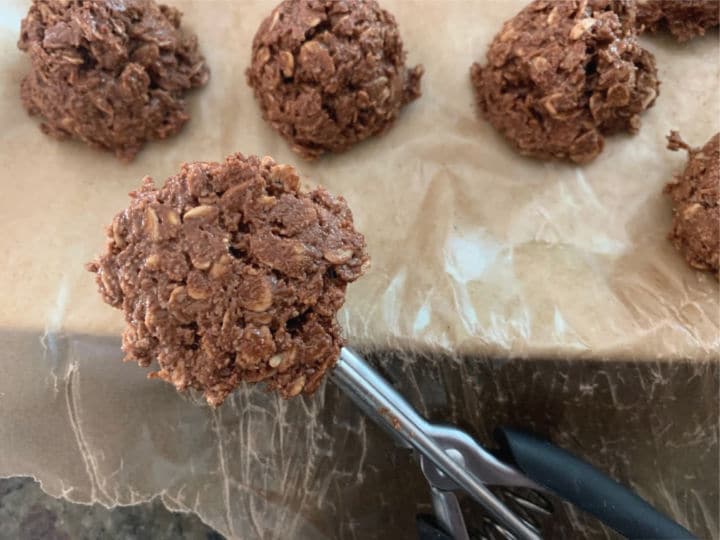 Using a cookie scoop to drop oat cookie onto a wax paper lined platter