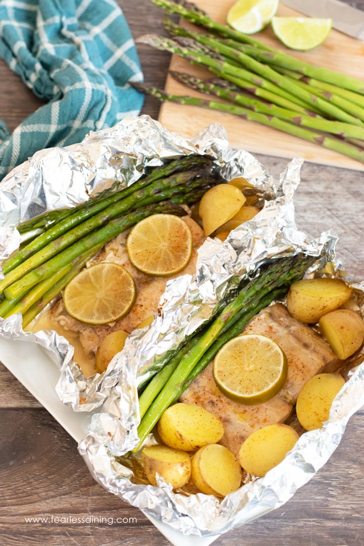 Two foil packets with mahi mahi and vegetables.