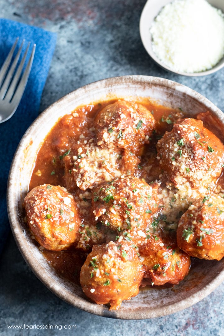The top view of a bowl of meatballs with pasta sauce. The meatballs are dusted with parmesan cheese and basil.