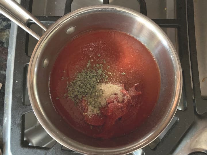 The tomato sauce, tomato paste, and spices in a pan on the stove.