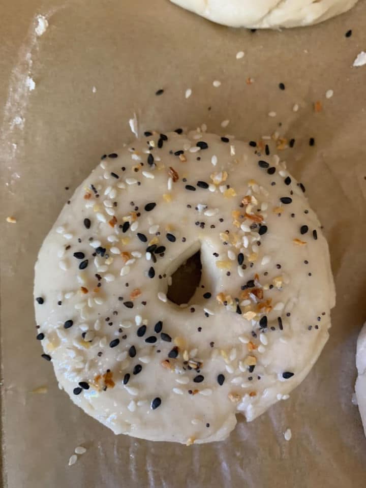 A single bagel topped with everything bagel mix ready to bake.