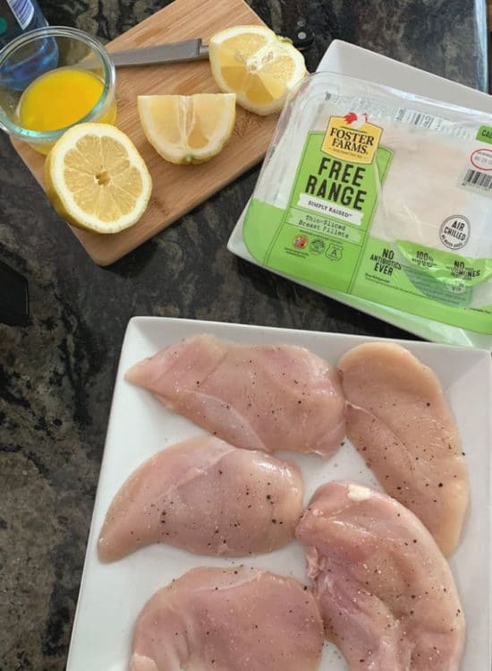 Raw chicken breasts on a plate with seasoning.