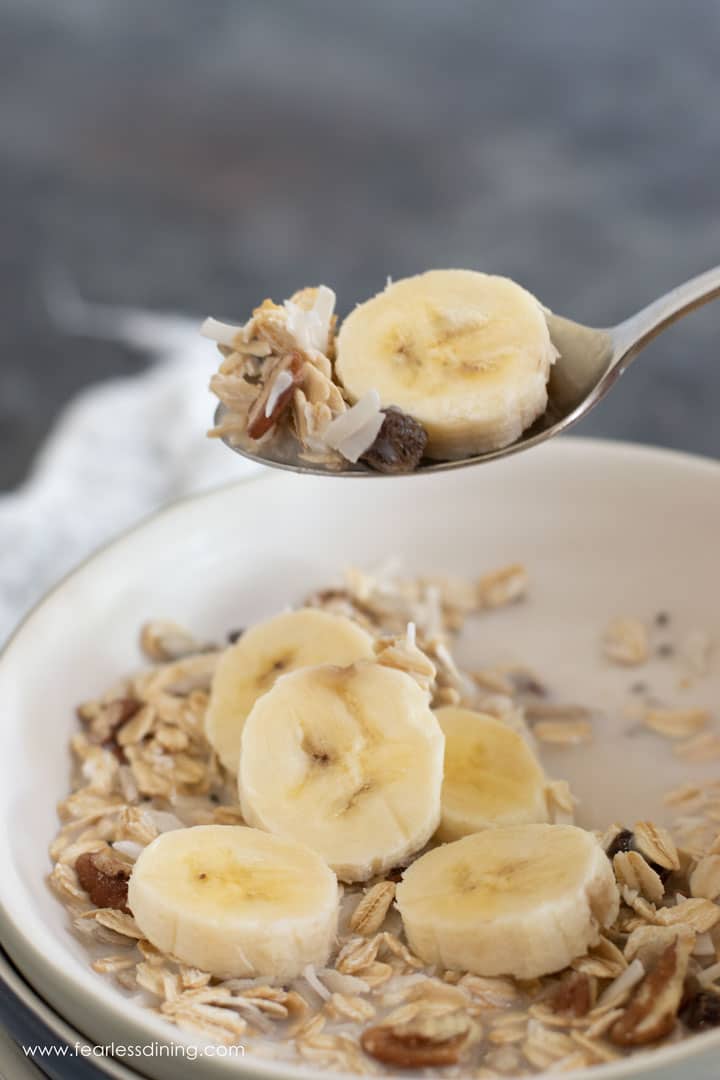 A spoon holding up a bite of muesli and sliced banana.