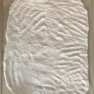 An oval shaped gluten free sourdough pizza crust on a baking sheet. It is ready to be baked.