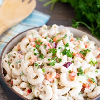A big bowl of deli style macaroni salad with a serving spoon and parsley.
