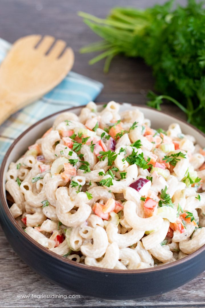 A big bowl of deli style macaroni salad with a serving spoon and parsley.