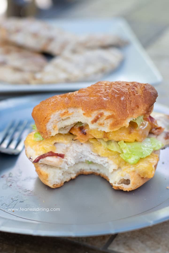 A grilled chicken burger on a paper plate. The burger has a bite taken out.