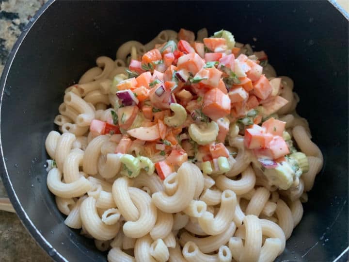 Adding the veggie mixture to the cooked macaroni.