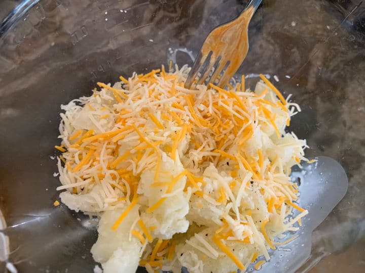 Adding the shredded cheese to the potatoes in a bowl.